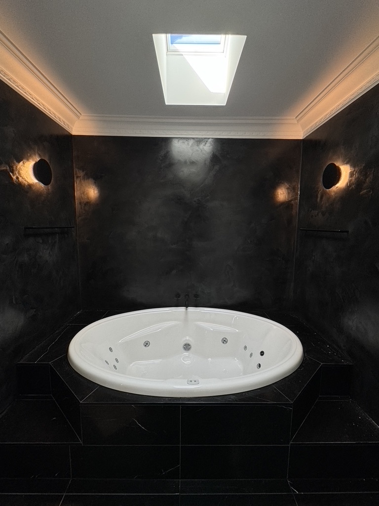 Dramatic black polished-plaster bathroom with spa bath from the Maroubra project by ACA Build